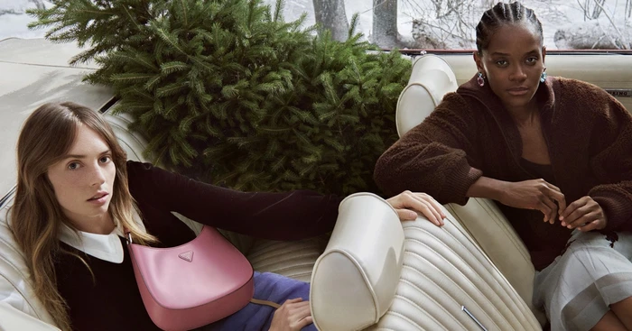 Maya Hawke and Letitia Wright seated inside a vintage car loaded with a pine tree for Prada Holiday 2025 campaign by Glen Luchford.