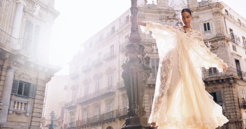 Model in a cream lace dress standing by an ornate street lamp in front of a historic European building