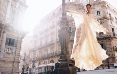 Model in a cream lace dress standing by an ornate street lamp in a public square with historic buildings