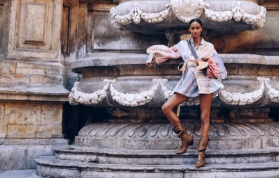 Model posing against a massive carved stone fountain wearing a striped shirt dress and slouchy boots