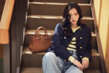 Jisoo sitting on indoor carpeted stairs wearing a blue blazer and striped sweater next to a brown leather handbag