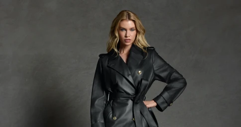 Stella Maxwell in a black leather belted trench coat against a textured grey background for Mackage CORE 2025.