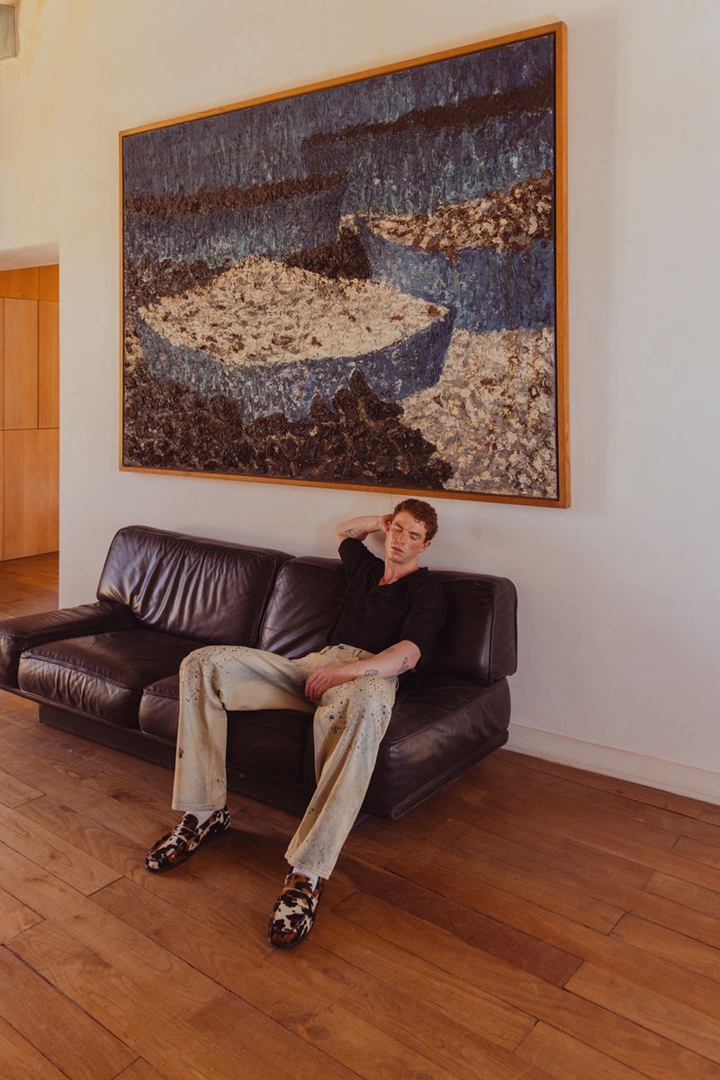 Adult male rests on black leather sofa in front of framed blue and white abstract artwork on wall inside a modern home interior.