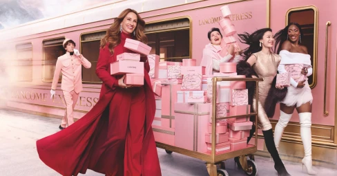 Julia Roberts holding pink boxes in front of a pink train alongside Isabella Rossellini, Ni Ni, and Aya Nakamura for Lancome Holiday 2025