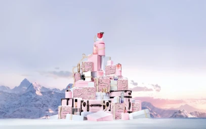 A towering pyramid of pink and white Lancôme gift boxes and perfume bottles set against a snowy mountain landscape at sunset.