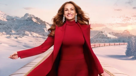 Julia Roberts wearing a red turtleneck and matching jacket, smiling with diamond earrings against a snowy mountain landscape