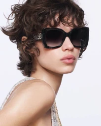 Model Mathilda Gvarliani wearing oversized black sunglasses and a textured tweed top against a clean white background.