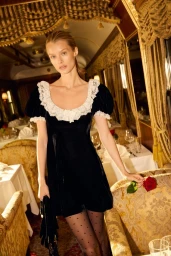Model Kris Grikaite in a black velvet dress with a lace collar holding a red rose in a luxury train car for For Love & Lemons.