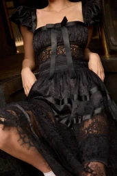 Model Kris Grikaite in a black lace dress with satin bows by For Love & Lemons