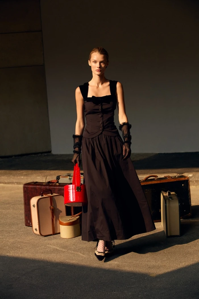 Model Kris Grikaite in a black dress with vintage suitcases for For Love & Lemons Winter 2025 by Camilla Akrans
