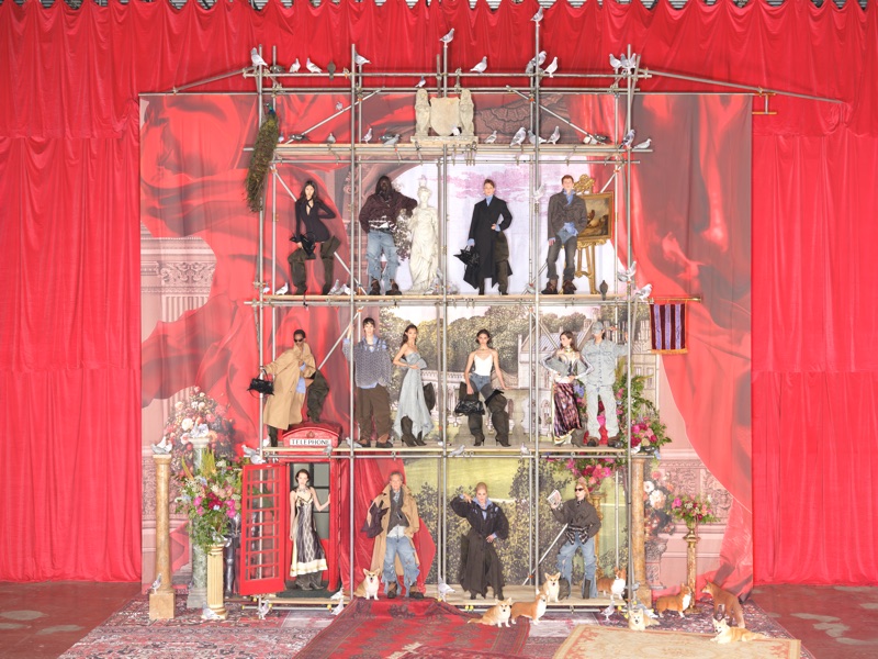 Models posed across multiple levels of scaffolding against a dramatic red curtain and painted classical backdrop for H&M.