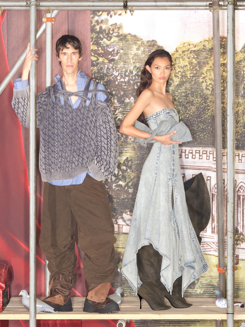 Two models posing within scaffolding structures against a painted pastoral backdrop for H and M by Glenn Martens