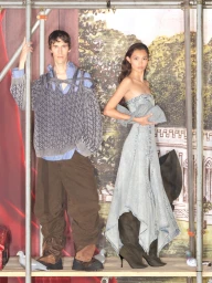 Two models posing within scaffolding structures against a painted pastoral backdrop for H and M by Glenn Martens