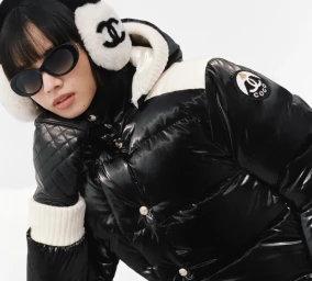 Nana Komatsu wearing a black puffer jacket, sunglasses, and white earmuffs against a seamless white background for Chanel Coco Neige.