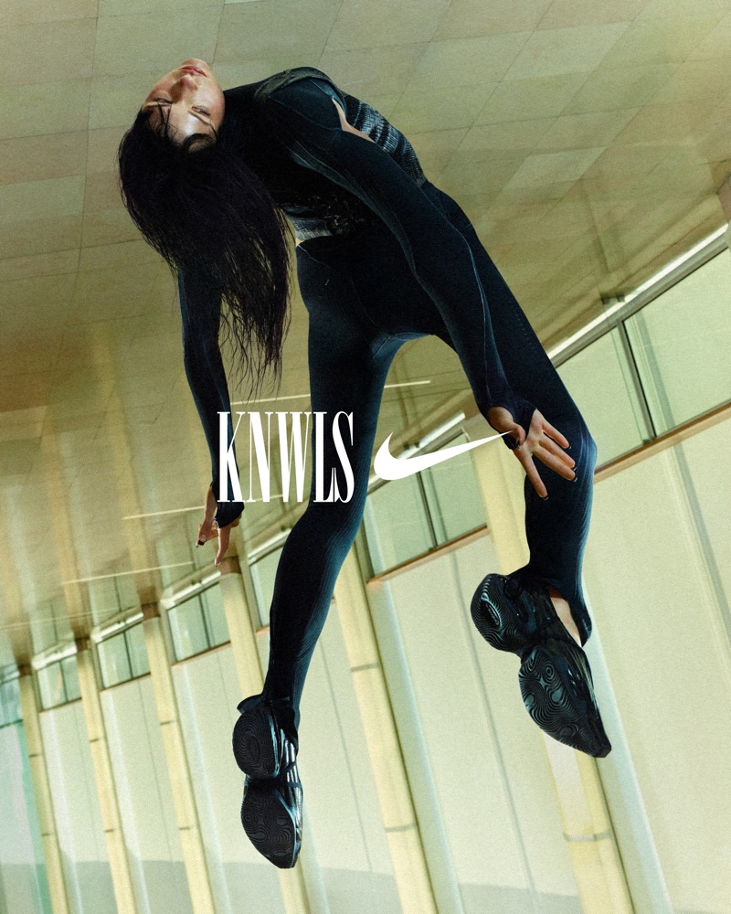 Model in black athletic bodysuit posing in an architectural hallway for the Nike x KNWLS collection campaign.