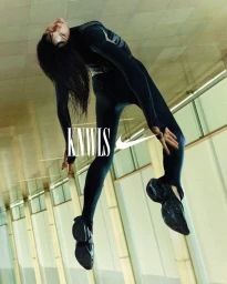 Model in black athletic bodysuit posing in an architectural hallway for the Nike x KNWLS collection campaign.