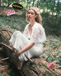 Model Apple Martin in a white lace dress seated on a fallen log in a lush forest for the Self-Portrait Fall-Winter 2025 campaign.