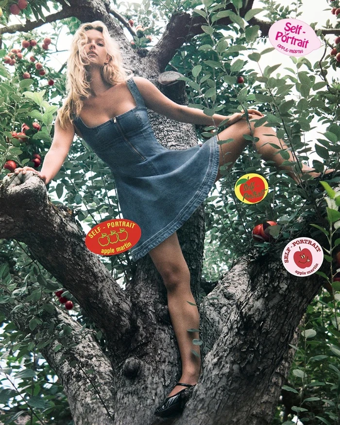 Model Apple Martin wearing a denim dress climbing an apple tree for Self-Portrait Fall-Winter 2025 campaign.