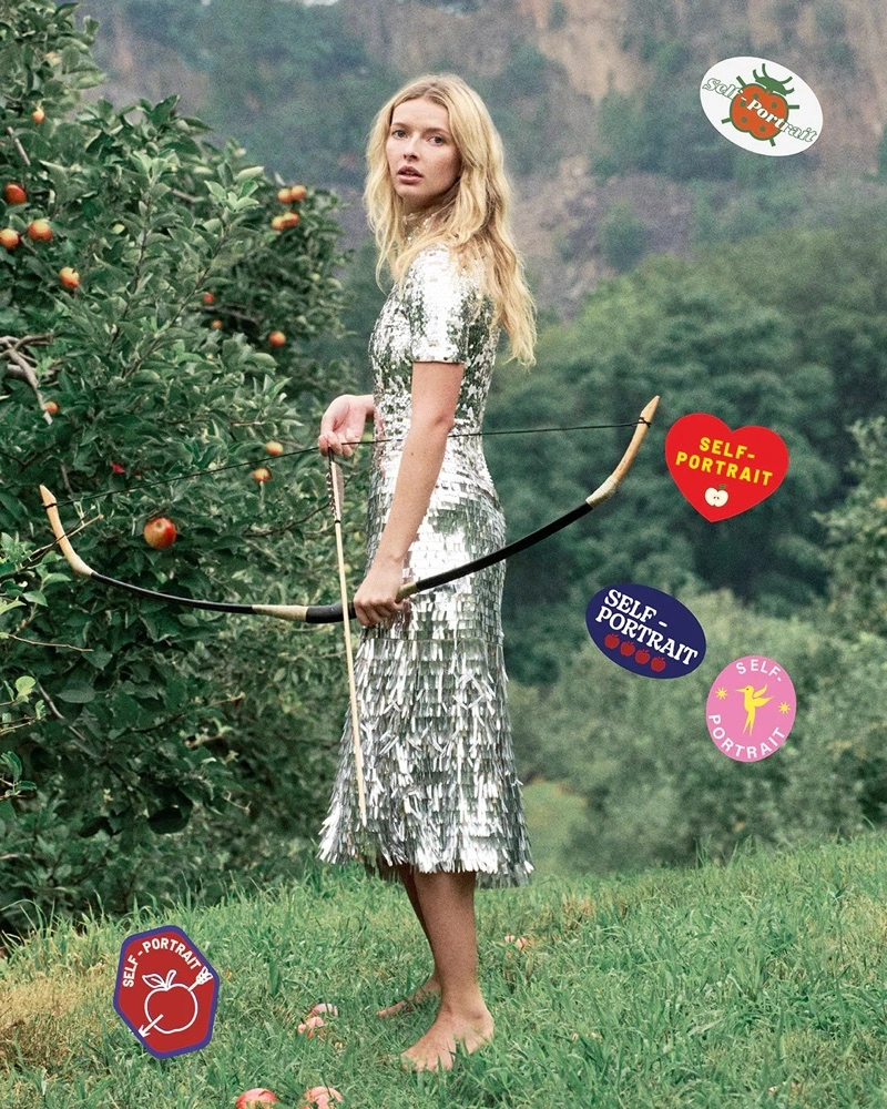 Apple Martin holding a bow and arrow wearing a silver sequin dress in an apple orchard for Self-Portrait