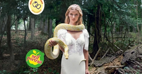 Model Apple Martin wearing a white lace dress with a yellow python snake draped over her shoulders in a forest setting.