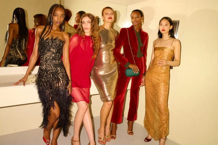 Five women in evening wear posing together in a lit room with mirrors for Saks Fifth Avenue photographed by Angelo Pennetta.