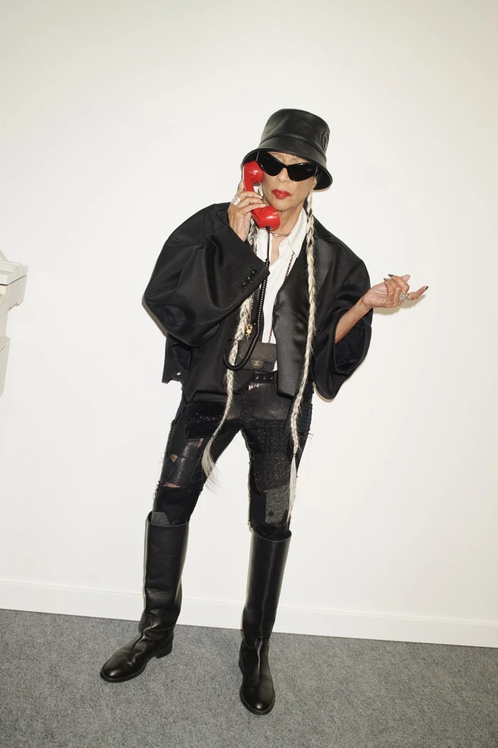 Model wearing a black bucket hat and oversized jacket holding a red telephone receiver against a plain white background