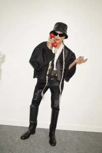 Model wearing a black bucket hat and oversized jacket holding a red telephone receiver against a plain white background