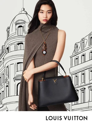 Hoyeon Jung in a brown sleeveless turtleneck holding a black leather handbag against a hand-drawn building backdrop