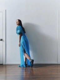 Model in a sheer blue tulle dress and black sneakers posing against a plain white wall