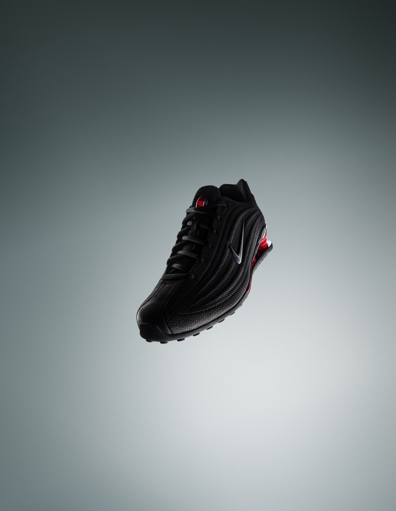 Black Nike Shox sneaker floating at an angle against a smooth grey gradient studio backdrop.