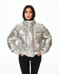 Kylie Jenner wearing a shiny silver puffer jacket and black leggings against a bright white background for Khy.