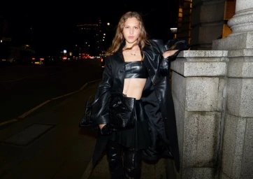 Model Angelina Kendall in a black leather outfit leaning against a stone building at night for H&M