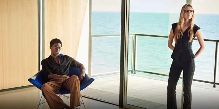 Two models wearing eyewear inside a modern room with ocean views for Oliver Peoples Malibu Forever