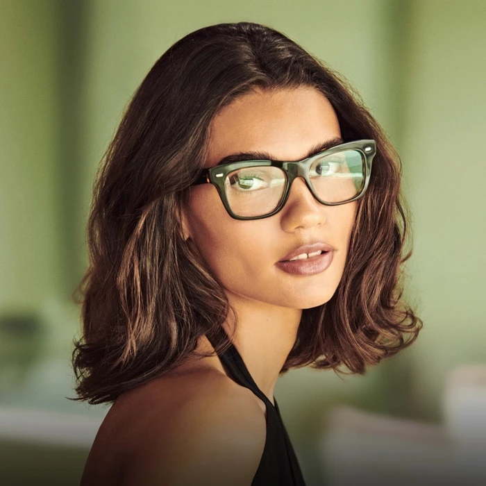 Model wearing dark glasses and a black top against a soft green background for Oliver Peoples Malibu Forever campaign.