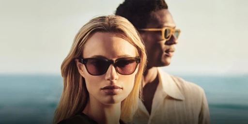 Close-up portrait of two models wearing sunglasses against an ocean backdrop for Oliver Peoples Malibu Forever campaign.