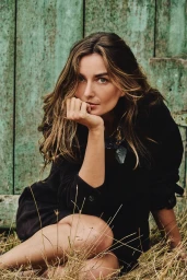 Model Andreea Diaconu posing outdoors in a black shirt against a weathered green wooden backdrop for Banana Republic