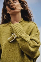 Model wearing a textured olive green knit sweater against a clear blue sky