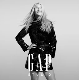 Gwyneth Paltrow wearing a black patent leather jacket and mini skirt against a light grey background