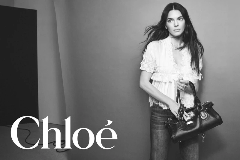 Black and white fashion portrait of Kendall Jenner holding a dark leather handbag in front of a grey backdrop for Chloe.
