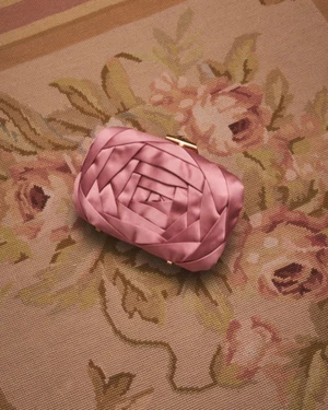 Pink satin rose-shaped clutch bag resting on a floral patterned rug for Roger Vivier campaign