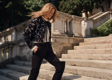 Model Doutzen Kroes walking down stone outdoor stairs wearing a patterned black jacket and dark trousers for Twinset.