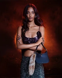 Model Mona Tougaard wearing a sequined top and skirt holding a black handbag with a furry charm against a dark backdrop.