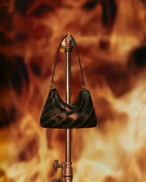 Rabanne black sequin shoulder bag hanging on a metallic stand against a warm abstract orange background