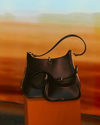 Two black leather handbags with gold hardware displayed on an orange pedestal against a warm blurred backdrop