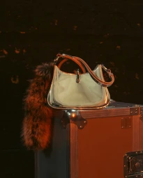 Glossy silver metallic handbag resting on a metallic flight case with a fluffy charm hanging off the side.