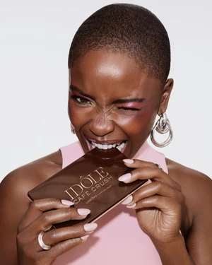 Close-up portrait of a woman with a buzzcut playfully biting into a chocolate eyeshadow palette for Lancome.