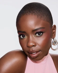 Close-up portrait of Joy Sunday with a buzz cut wearing silver hoop earrings and a pink top against a white backdrop.
