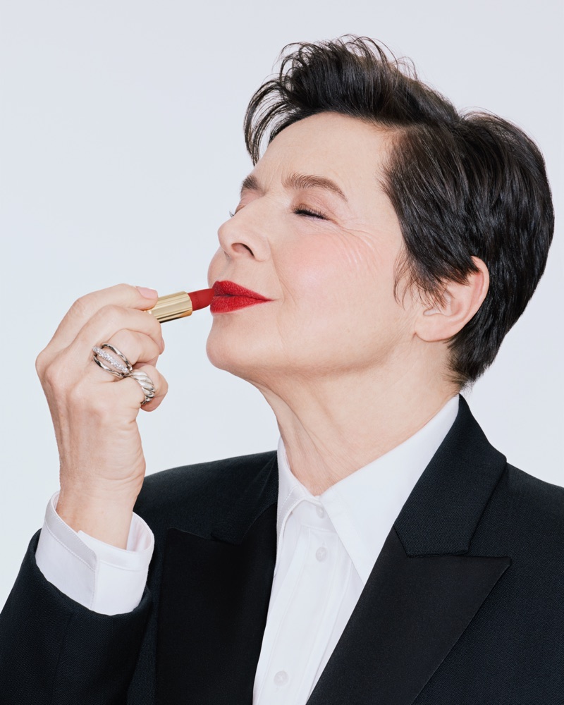 Isabella Rossellini applying red lipstick wearing a black suit jacket and white shirt against a white backdrop for Lancome