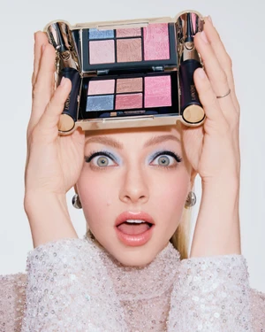 Amanda Seyfried holding a Lancôme makeup palette above her head against a white seamless background
