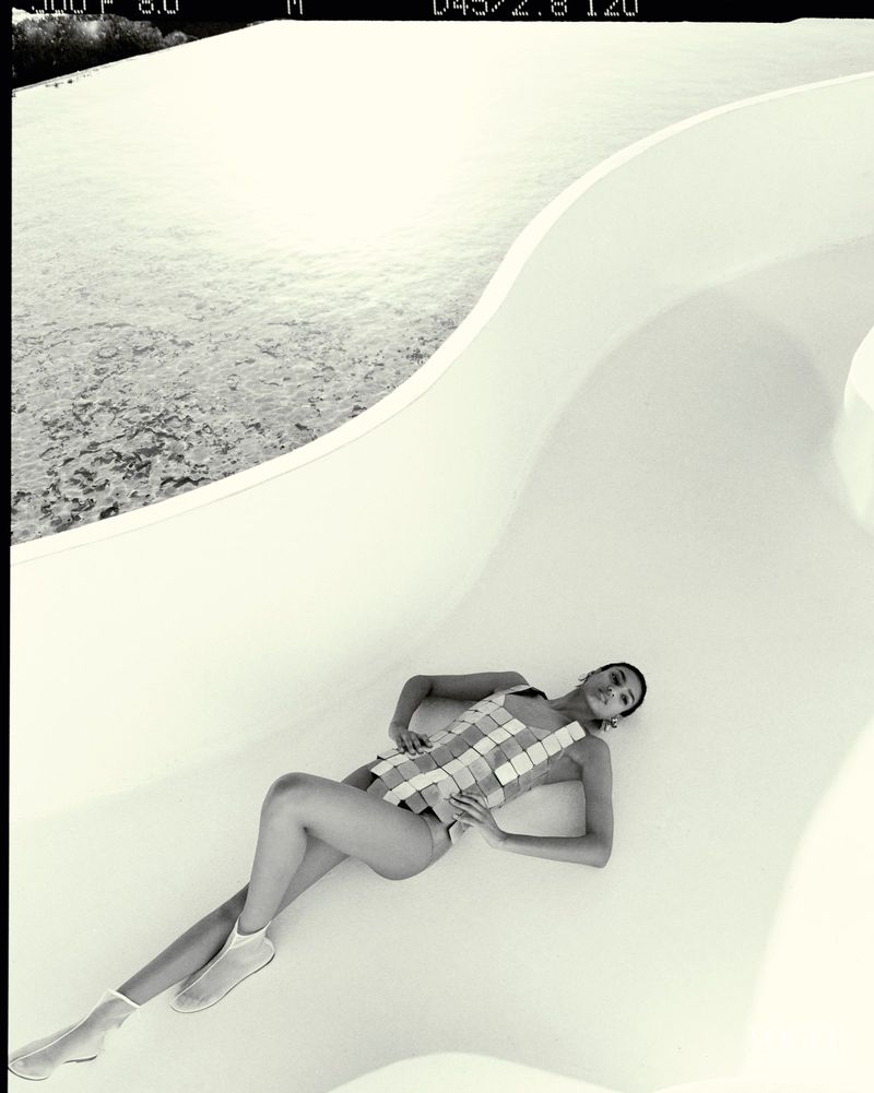 Fashion shot of a woman in a swimsuit and booties lying on a white slide. Black and white photography with an overhead camera angle.